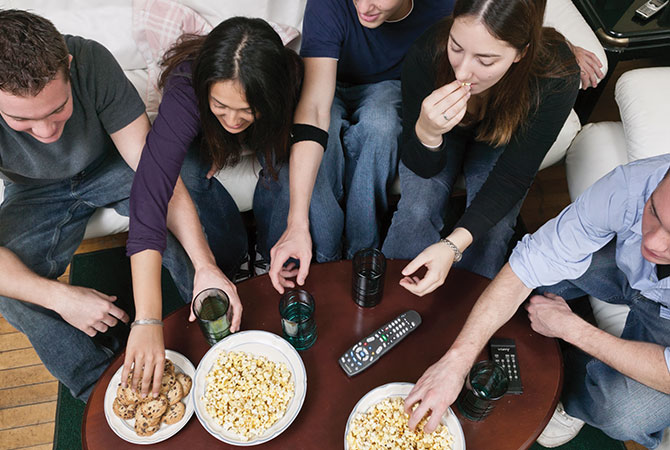 a group of friends sitting around a table eating cookies and popcorn