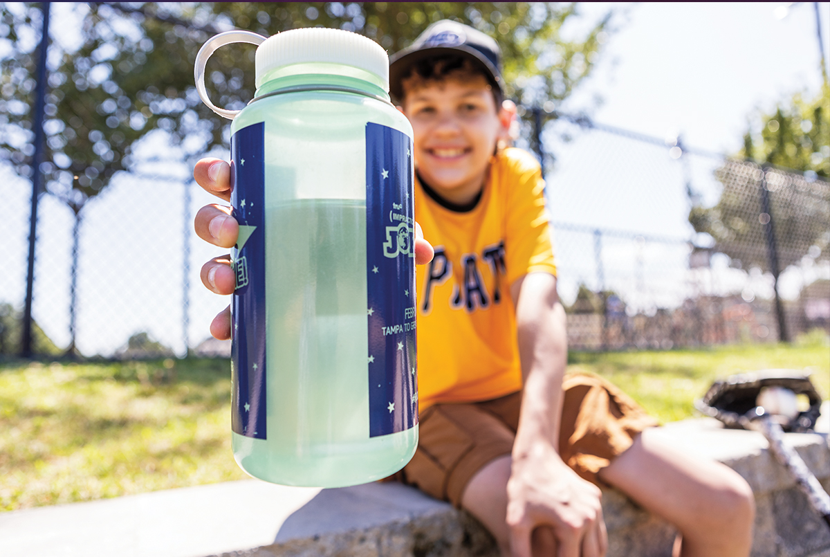 Kid at a field with water bottle extended toward the camera
