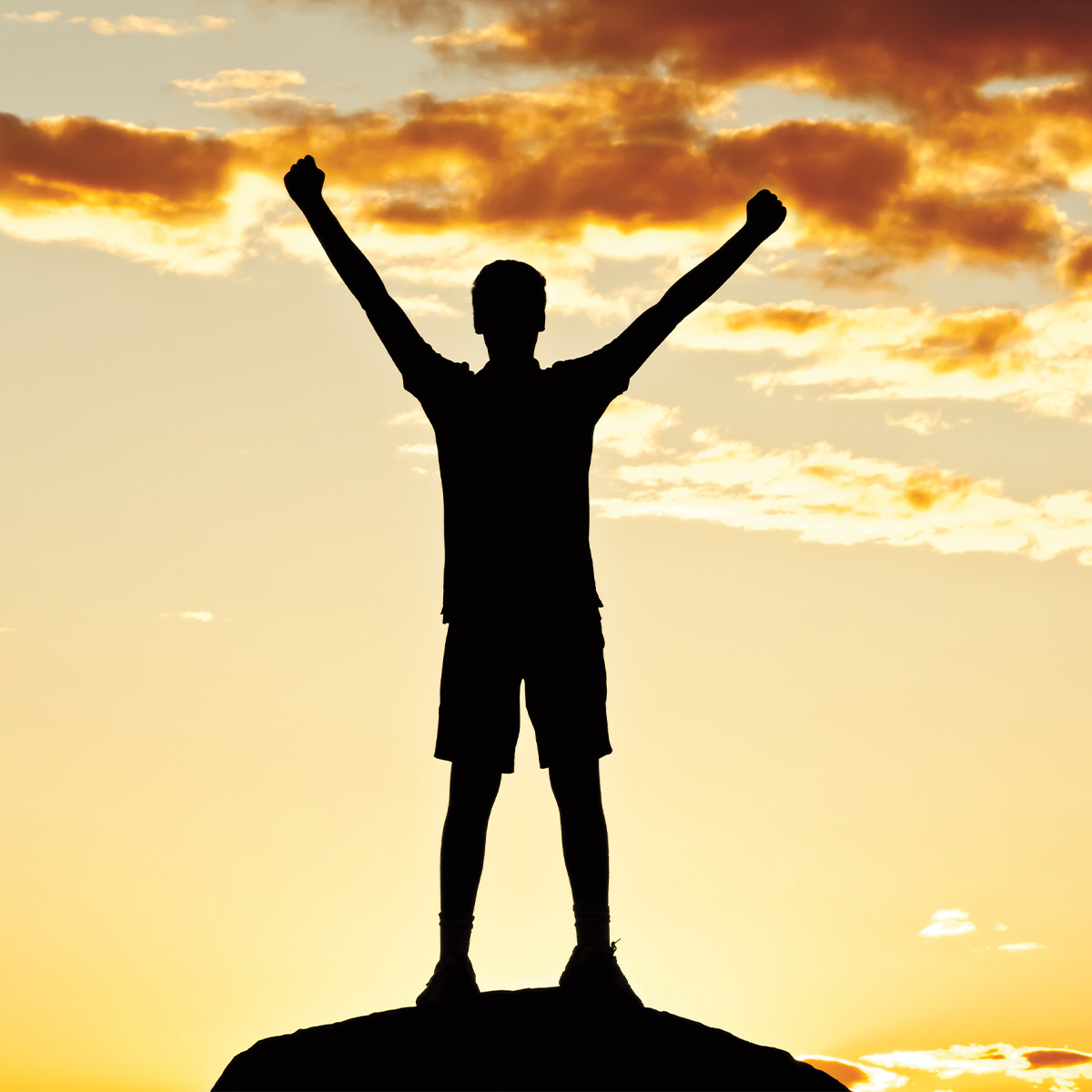 Photo of a silhouetted person cheering on top of a hill