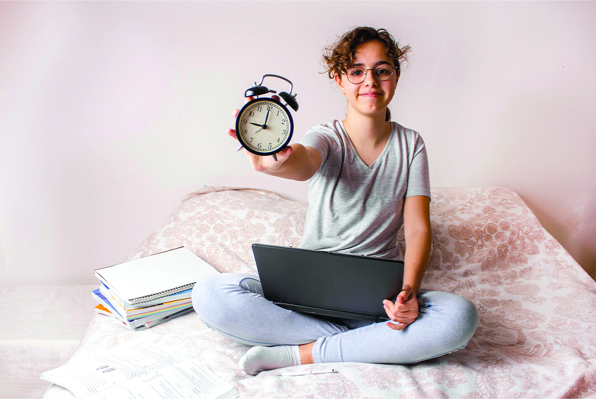 Image of teen holding an alarm clock and their laptop