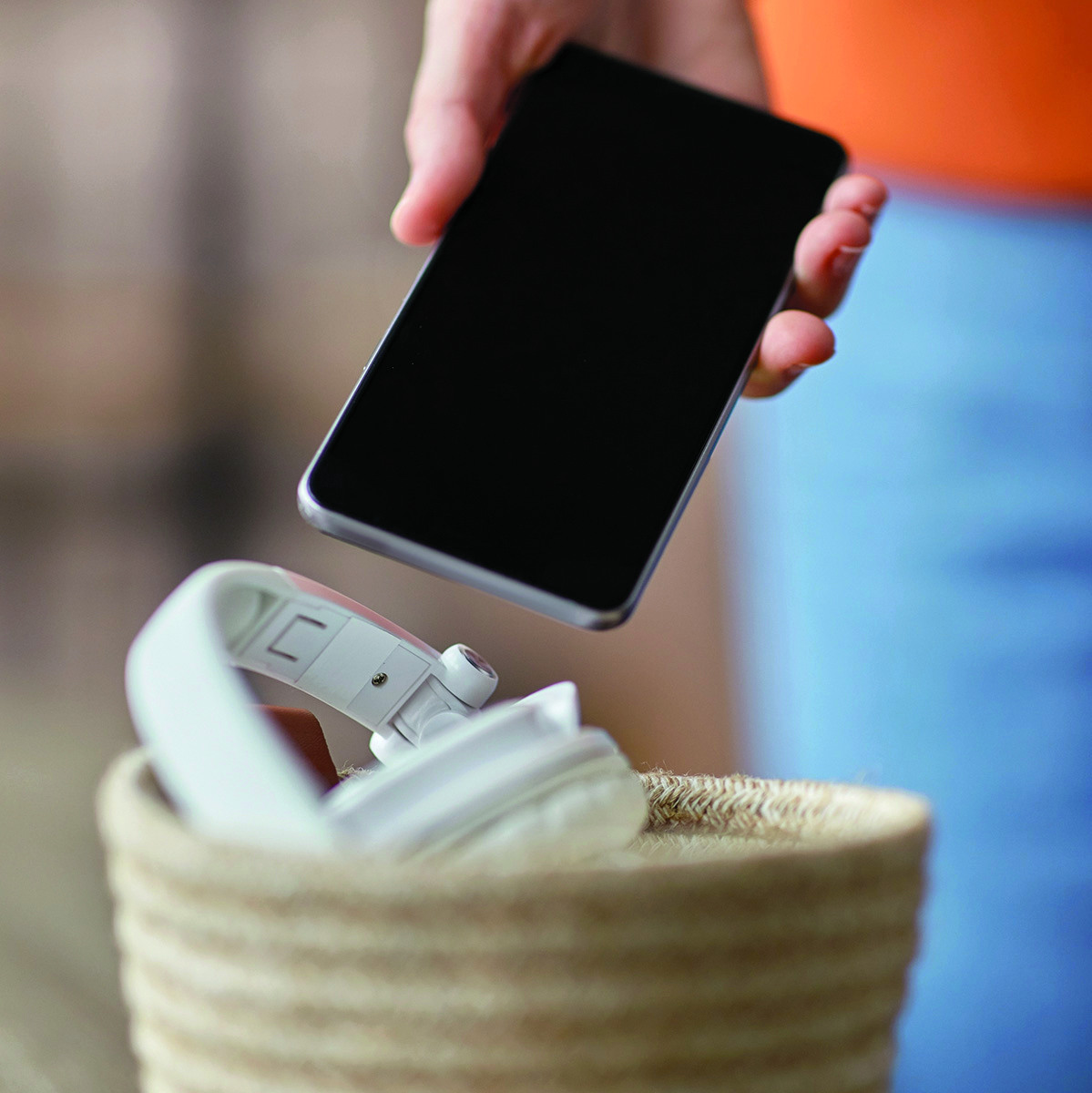 Image of a cellphone and headphones being placed into a basket