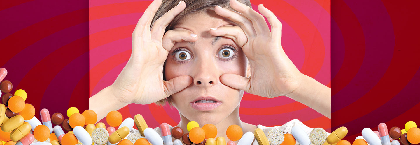 A person holds their hands around their wide-open eyes with pills and capsules scattered below