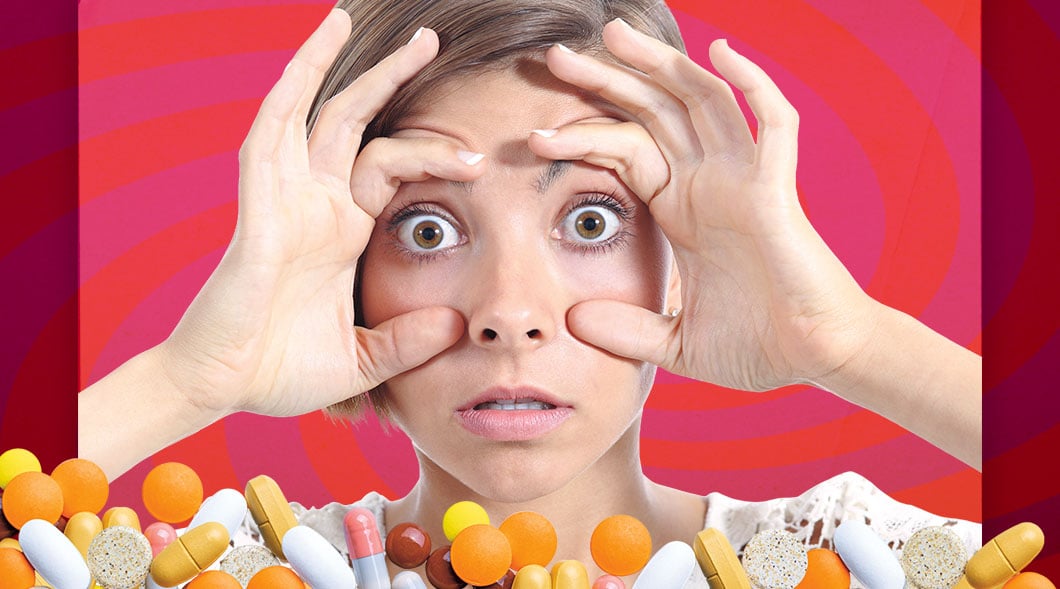 A woman with wide eyes holds her hands to her face with various pills and capsules below