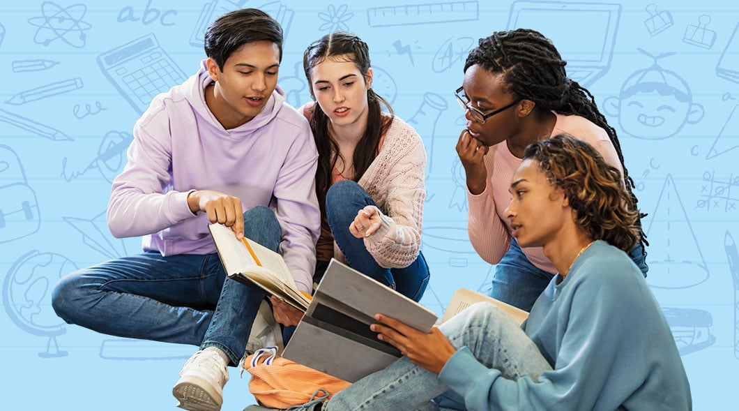 Four students sit together and review open books and notebooks as a group