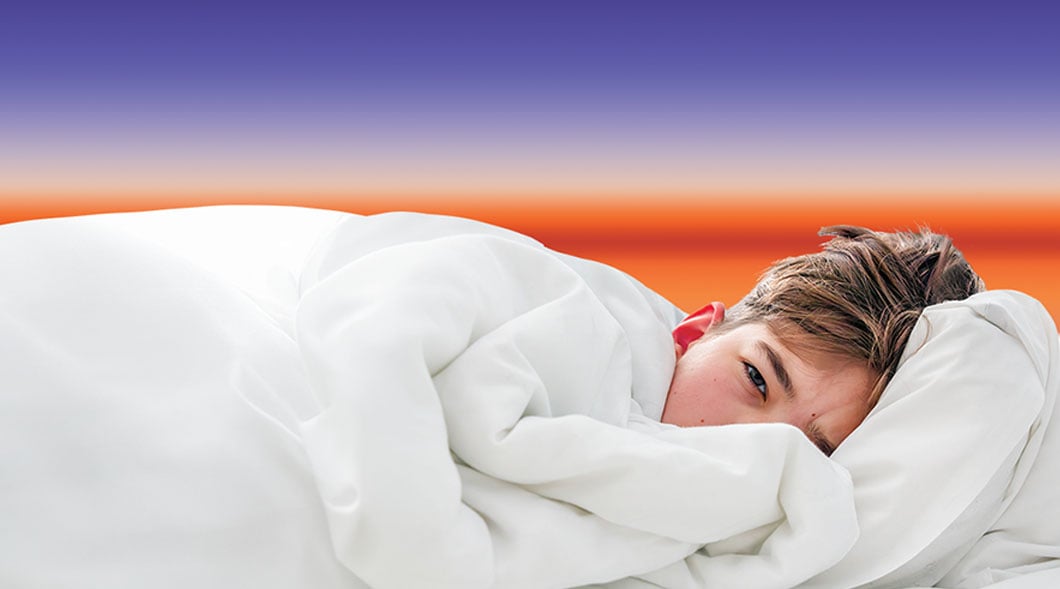 A child lies in bed wrapped in white blankets with eyes open