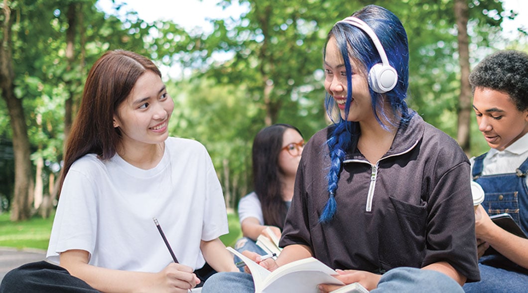 A group of students sit outdoors and look at an open book together