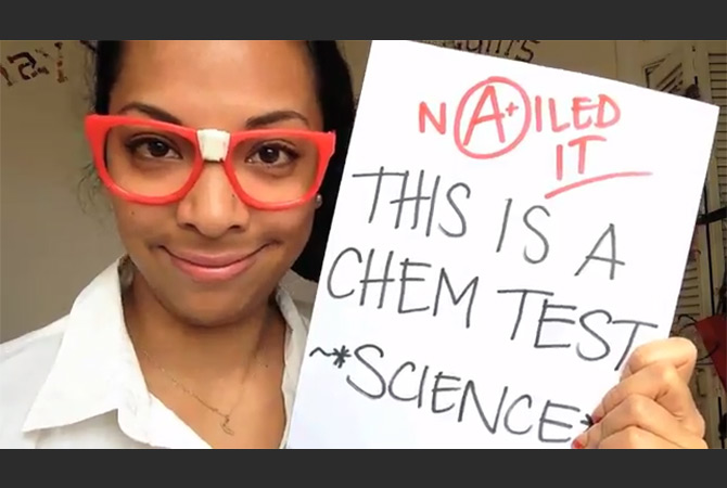 A woman with glasses holding a chemistry test she passed.