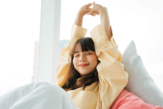 enlargeable photo: a  girl stretches her arms over her head while in bed